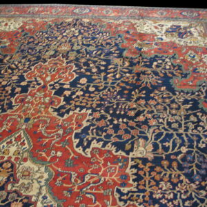 Intricate low-pile rug featuring dense floral motifs in indigo blue, terracotta red, and cream.