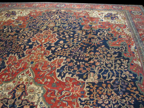 Intricate low-pile rug featuring dense floral motifs in indigo blue, terracotta red, and cream.