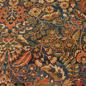 Ornate floral rug pattern with deep blue field, rust orange, gold, and olive green motifs.