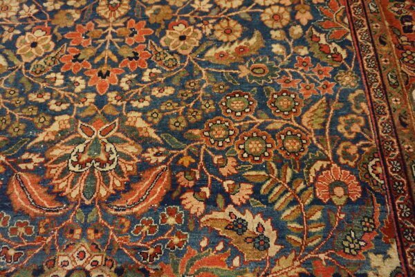Ornate floral rug pattern with deep blue field, rust orange, gold, and olive green motifs.