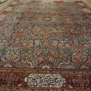 Large blue rug with a dense traditional floral pattern and rust borders featuring script cartouches on a wood floor.