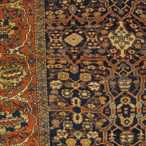 A highly detailed oriental rug corner in navy, rust, and gold lies against pale wood flooring.