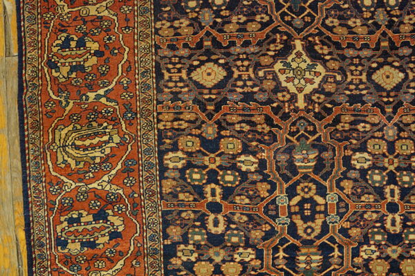 A highly detailed oriental rug corner in navy, rust, and gold lies against pale wood flooring.