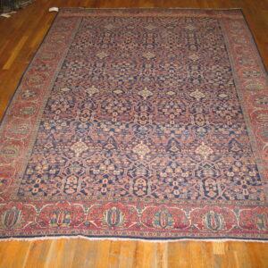 Dark blue patterned rug with repeating motifs and wide red borders rests on brown hardwood floors.