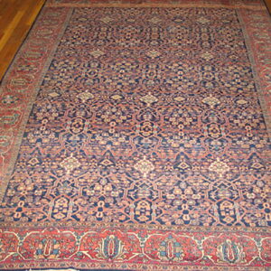 Large, patterned low-pile rug in dark blue and rust red lies on polished hardwood floorboards.