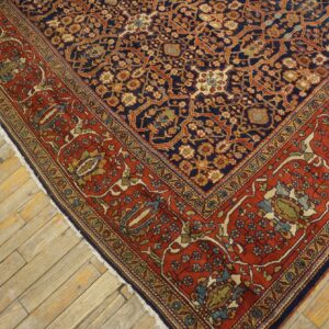 Intricate floral rug with a navy center and wide rust border rests on distressed light wood floorboards.