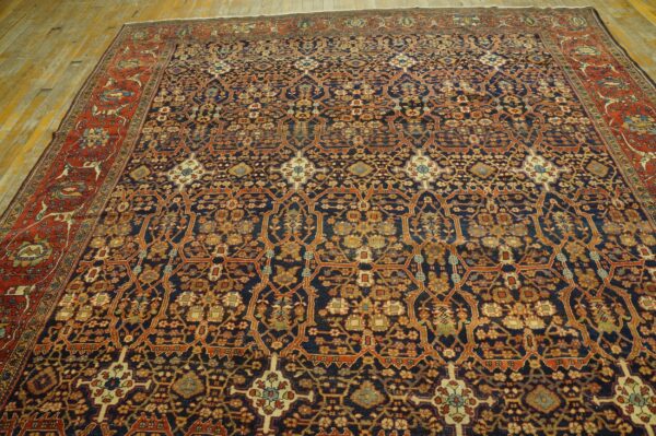 Low-pile rug with a detailed dark blue trellis pattern and wide rust border on plank wood flooring.
