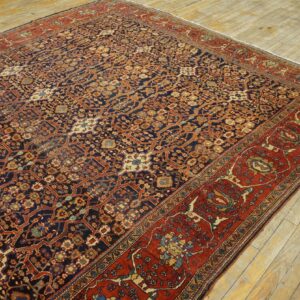 Dark blue patterned rug with red and terracotta accents displayed on weathered light hardwood flooring.