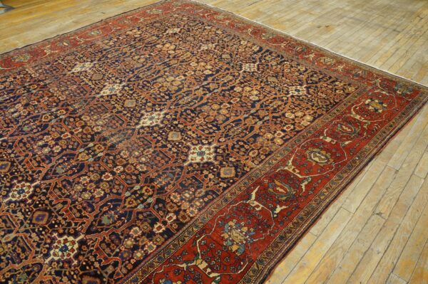 Dark blue patterned rug with red and terracotta accents displayed on weathered light hardwood flooring.