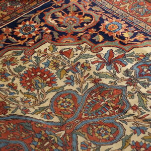 The detailed rug displays a cream field with red and blue floral patterns next to a dark navy border.