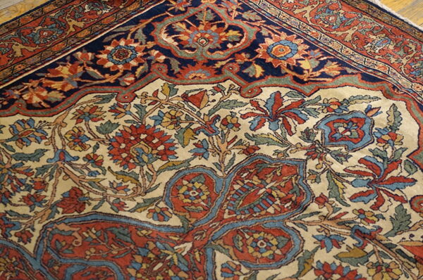The detailed rug displays a cream field with red and blue floral patterns next to a dark navy border.