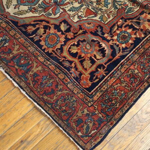 Ornate navy and rust patterned rug corner with cream accents resting on light wood planks.