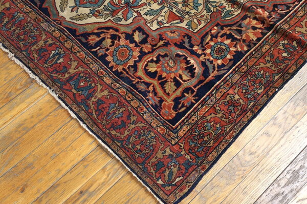 Ornate navy and rust patterned rug corner with cream accents resting on light wood planks.