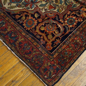 Low-pile rug corner with intricate navy, red, and gold floral patterns rests on distressed hardwood flooring.