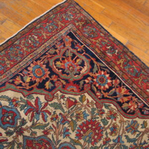 Multicolored high-detail floral rug corner with navy medallion and red borders resting on a wooden floor.