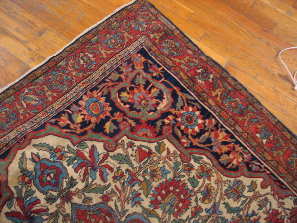 Multicolored high-detail floral rug corner with navy medallion and red borders resting on a wooden floor.