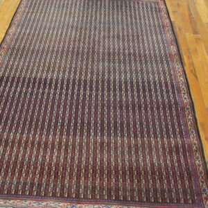 Red and dark blue rug with repeating vertical striped patterns rests on a polished hardwood floor.