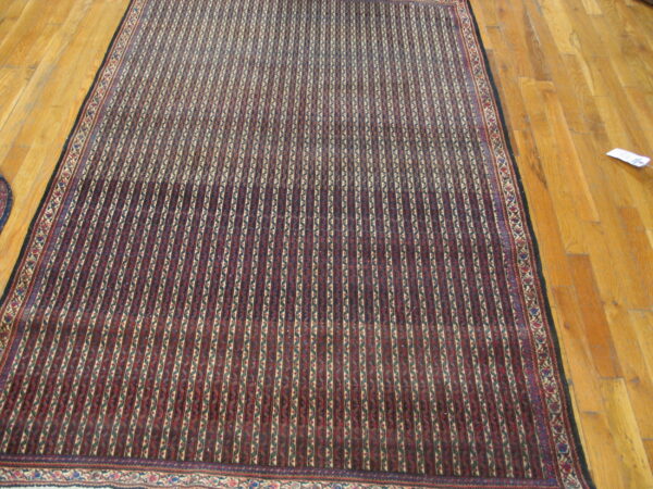 Red and dark blue rug with repeating vertical striped patterns rests on a polished hardwood floor.