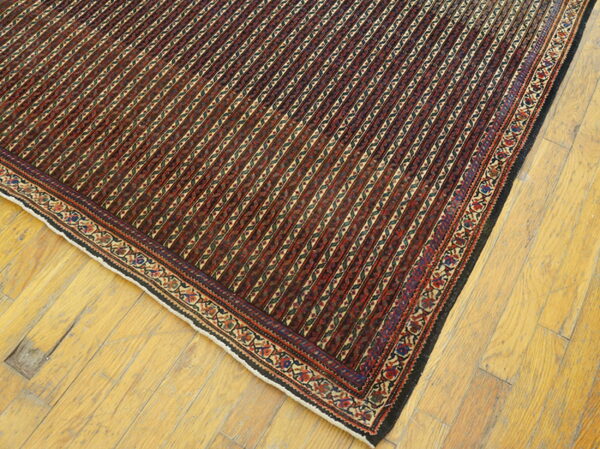 Dark red and black striped rug with intricate geometric borders covers a section of worn wood flooring.