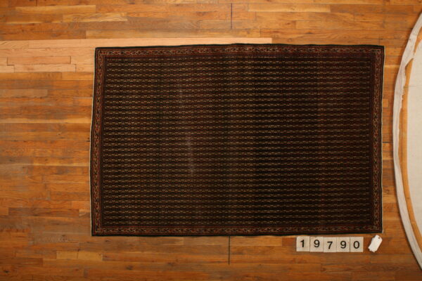 Dark rectangular rug featuring dense horizontal geometric rows and a patterned border on natural wood flooring.