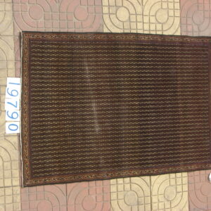 Dark brown rug with horizontal striped geometric patterns and a detailed border, lying on patterned concrete tile.