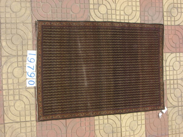 Dark brown rug with horizontal striped geometric patterns and a detailed border, lying on patterned concrete tile.