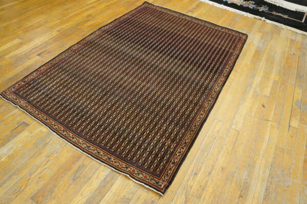 Burgundy and black geometric striped rug displayed on aged, light-colored wood flooring.