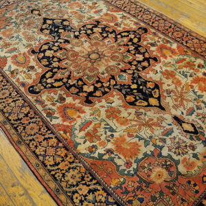 Ornate floral and medallion rug in navy, cream, and orange on distressed wooden floorboards.