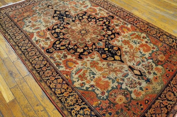 Ornate floral and medallion rug in navy, cream, and orange on distressed wooden floorboards.