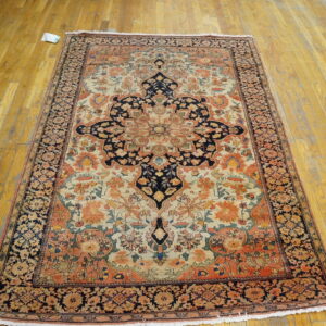 Low-pile rug with navy, coral, and cream floral medallion design laid on worn wooden planks.