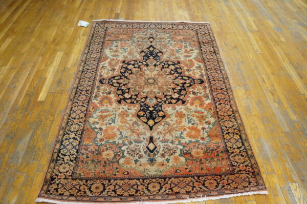 Low-pile rug with navy, coral, and cream floral medallion design laid on worn wooden planks.