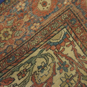 Detail shot of a low-pile rug featuring a complex red, tan, and blue traditional geometric pattern.