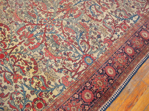 Detailed beige, red, and blue traditional rug with a wide navy floral border resting on wood planks.
