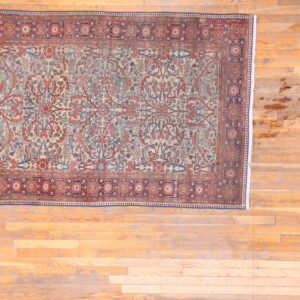 Traditional rug with cream, red, and blue foliate designs and complex borders on wood flooring.