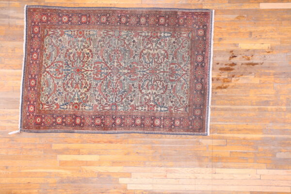 Traditional rug with cream, red, and blue foliate designs and complex borders on wood flooring.