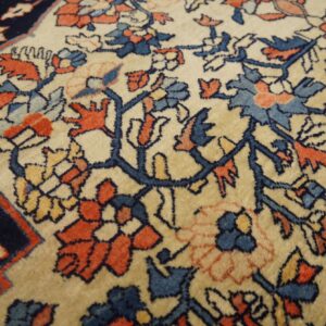 Close-up of a floral rug with a cream field and motifs in navy, rust, and dusty blue.