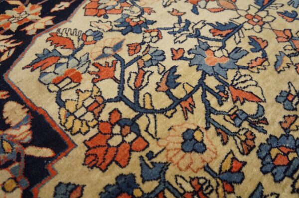 Close-up of a floral rug with a cream field and motifs in navy, rust, and dusty blue.