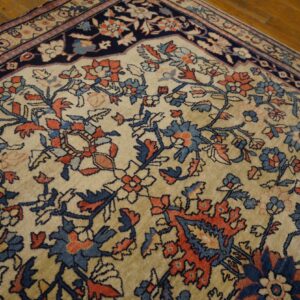 Beige traditional rug corner with detailed navy and rust floral motifs on a hardwood floor.