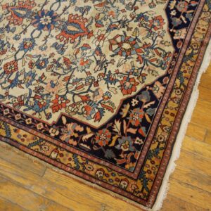 Traditional ivory rug with navy, rust, and gold floral patterns rests on distressed wood floorboards.