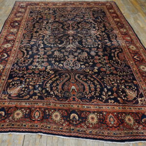 Intricate navy rug with complex floral designs and a wide rust-red patterned border on wood floors.