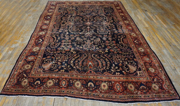 Intricate navy rug with complex floral designs and a wide rust-red patterned border on wood floors.