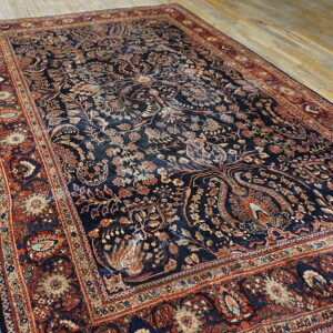 Ornate navy rug with low pile, detailed rust and beige borders, displayed on light wooden floorboards.