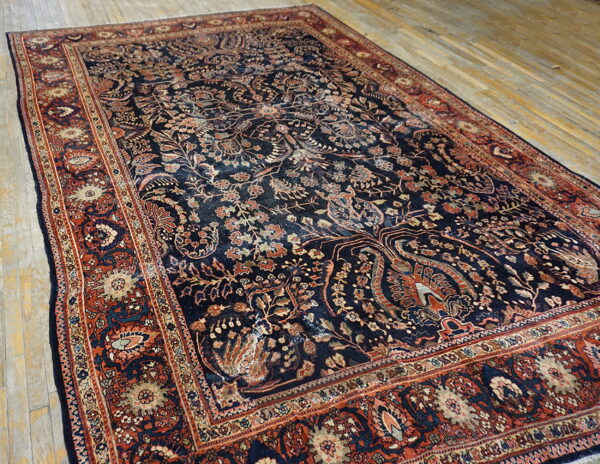 Ornate navy rug with low pile, detailed rust and beige borders, displayed on light wooden floorboards.
