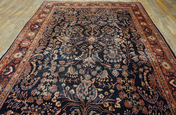 A large, intricately patterned navy rug with rust-red borders lies on light wooden plank floors.
