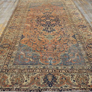 Orange, navy, and tan rug with a traditional medallion pattern rests on gray wood flooring.