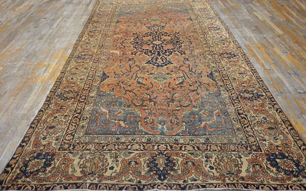 Orange, navy, and tan rug with a traditional medallion pattern rests on gray wood flooring.