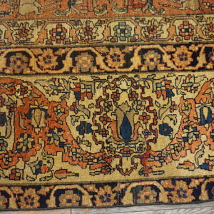 Ornate traditional rug border in navy, orange, and beige rests on distressed wood flooring.
