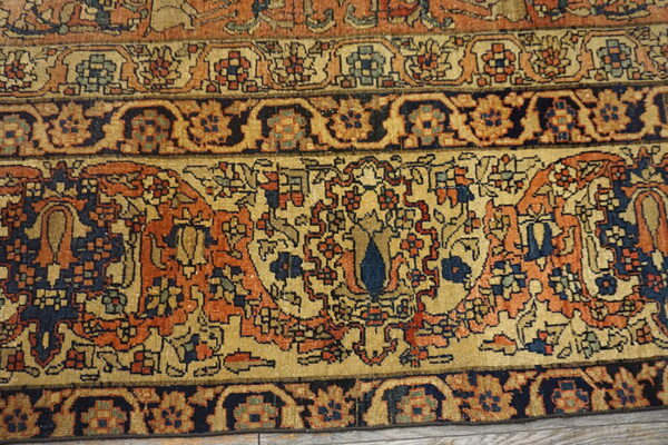 Ornate traditional rug border in navy, orange, and beige rests on distressed wood flooring.