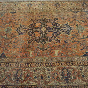 Terracotta rug with an ornate dark blue medallion, intricate borders, and visible low pile floral texture.
