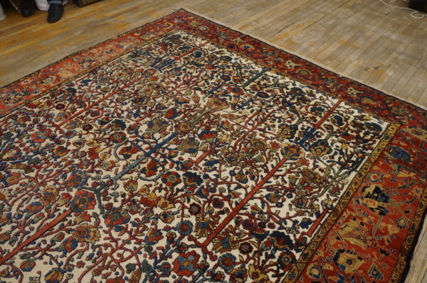 Traditional rug with dense red, blue, and gold floral pattern on an ivory ground, displayed on wood planks.